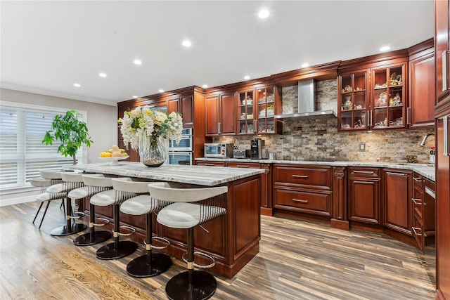 bar area featuring wall chimney range hood, stainless steel double oven, backsplash, wood finished floors, and recessed lighting
