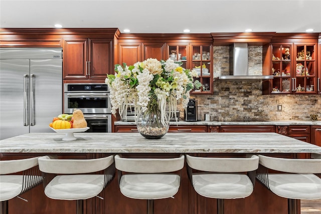 kitchen with wall chimney exhaust hood, stainless steel appliances, a kitchen breakfast bar, backsplash, and recessed lighting