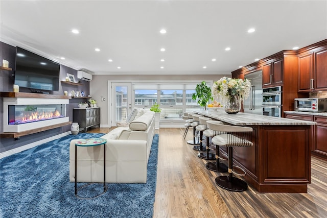 living area with an AC wall unit, ornamental molding, wood finished floors, recessed lighting, and a glass covered fireplace