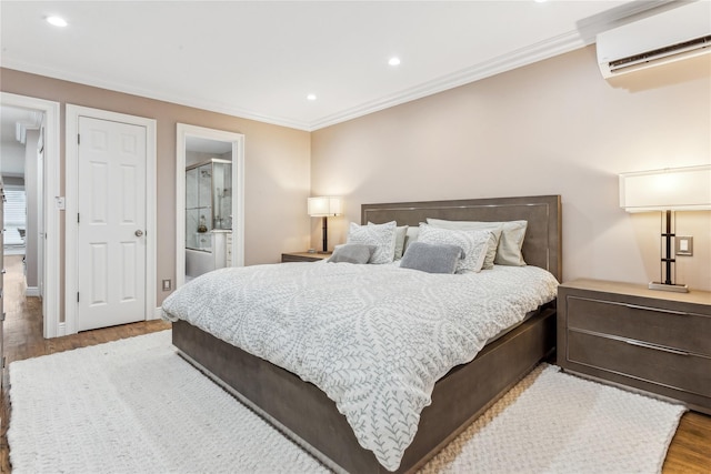 bedroom with an AC wall unit, wood finished floors, recessed lighting, ornamental molding, and connected bathroom