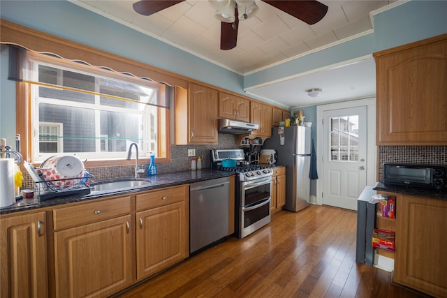 kitchen featuring crown molding, appliances with stainless steel finishes, sink, hardwood / wood-style flooring, and dark stone countertops