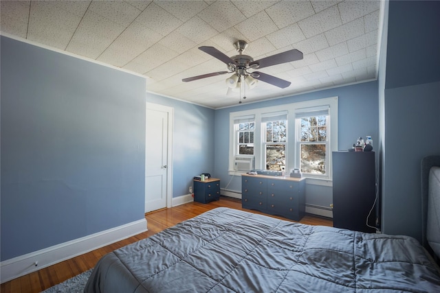 bedroom featuring ceiling fan, baseboard heating, hardwood / wood-style flooring, and ornamental molding