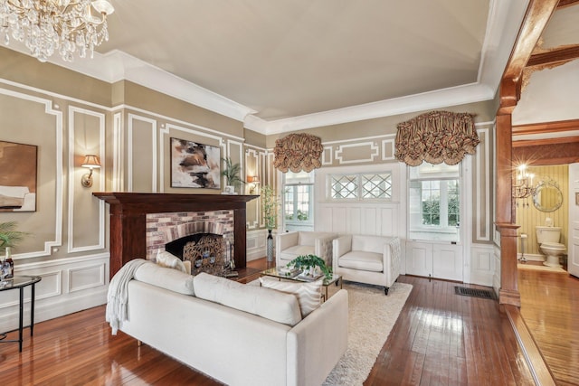 living room featuring an inviting chandelier, crown molding, a fireplace, and wood-type flooring