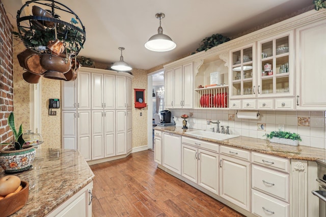 kitchen featuring sink, tasteful backsplash, light stone counters, light wood-type flooring, and pendant lighting