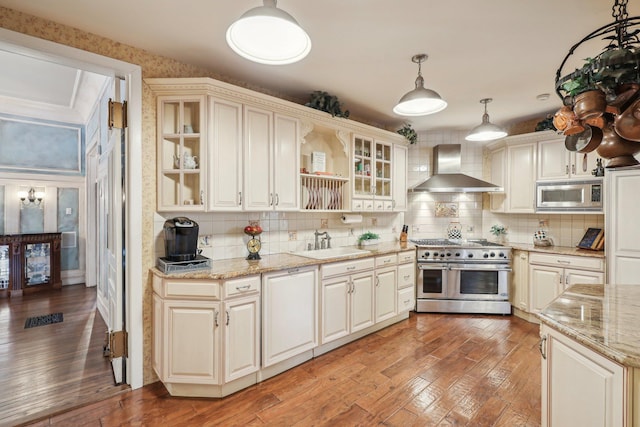 kitchen with pendant lighting, wall chimney range hood, backsplash, and appliances with stainless steel finishes