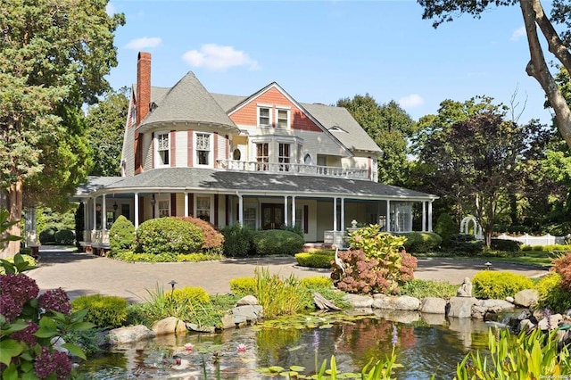 view of front of property with a balcony, a chimney, a shingled roof, and a small pond