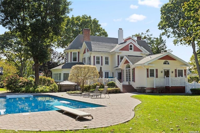 rear view of house with an outdoor pool, a lawn, and a patio
