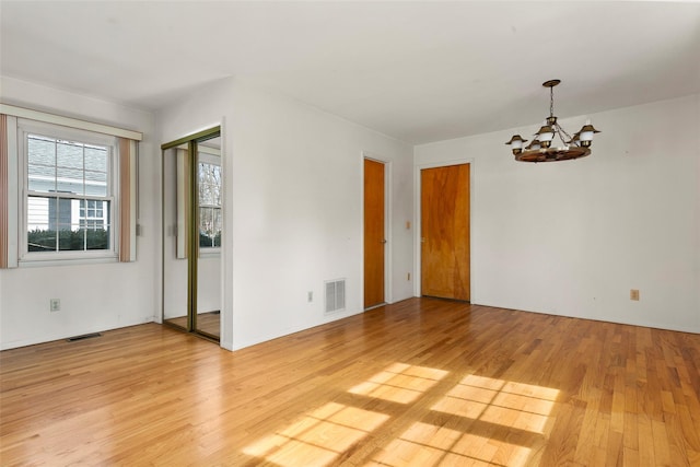 spare room with light wood finished floors, visible vents, and a notable chandelier