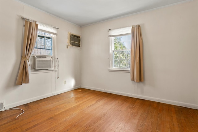 spare room featuring baseboards, ornamental molding, a wall unit AC, and light wood-style floors