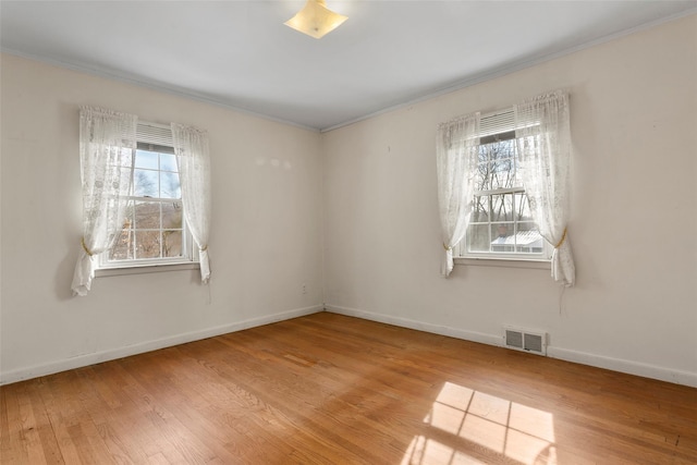 spare room with a wealth of natural light, wood finished floors, visible vents, and baseboards