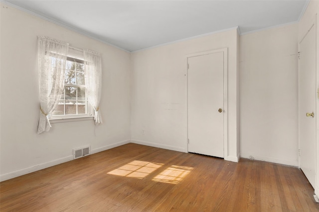 empty room with baseboards, crown molding, visible vents, and wood finished floors