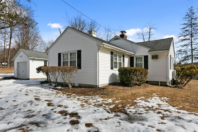 snow covered property featuring a shingled roof, a chimney, a detached garage, and an outdoor structure