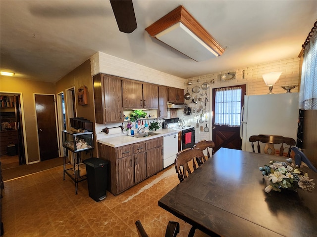 kitchen featuring dark brown cabinetry, brick wall, sink, and white appliances