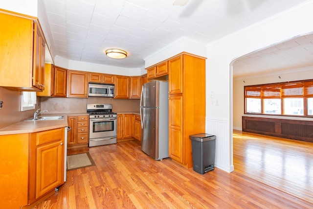 kitchen featuring appliances with stainless steel finishes, radiator, sink, ornamental molding, and light wood-type flooring