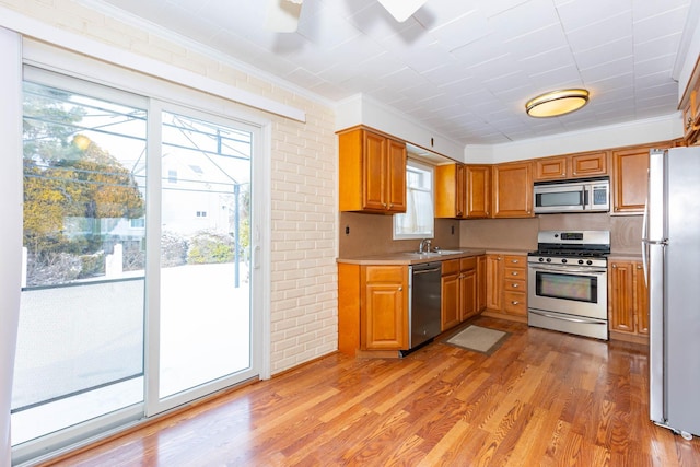 kitchen with crown molding, appliances with stainless steel finishes, brick wall, sink, and light hardwood / wood-style flooring