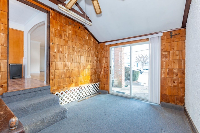 unfurnished living room with carpet, wooden walls, ornamental molding, and vaulted ceiling