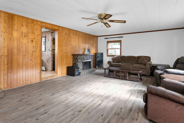 living room with wood walls, wood-type flooring, ornamental molding, and a stone fireplace