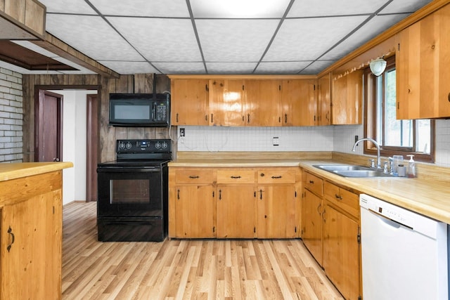 kitchen featuring a paneled ceiling, black appliances, tasteful backsplash, sink, and light wood-type flooring