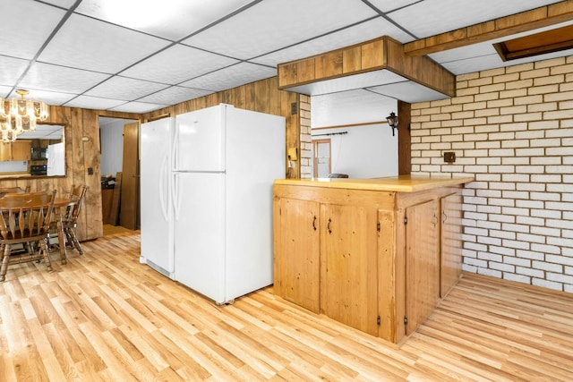 kitchen with kitchen peninsula, white refrigerator, light wood-type flooring, brick wall, and a drop ceiling