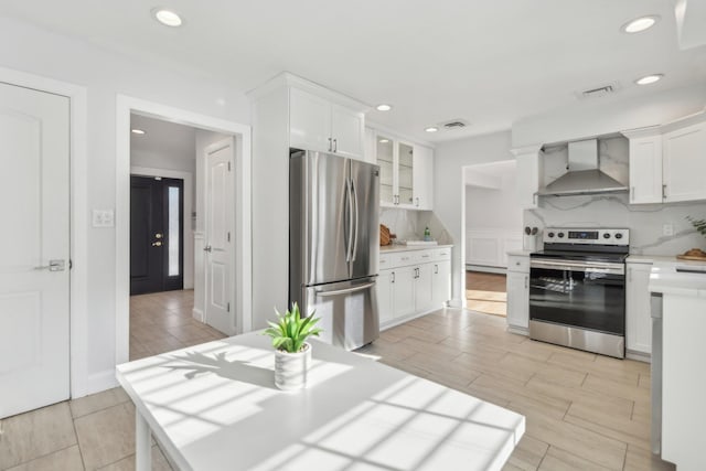 kitchen with decorative backsplash, white cabinets, wall chimney range hood, and appliances with stainless steel finishes