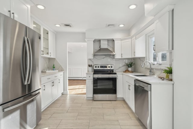 kitchen featuring appliances with stainless steel finishes, wall chimney exhaust hood, sink, white cabinetry, and tasteful backsplash