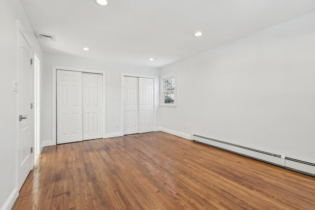 unfurnished bedroom featuring multiple closets, a baseboard heating unit, and hardwood / wood-style floors