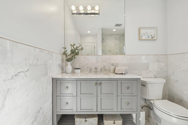 bathroom featuring a shower with door, toilet, vanity, and tile walls