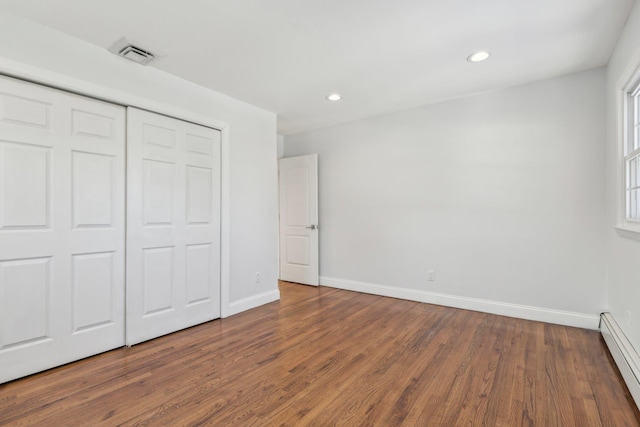 unfurnished bedroom featuring baseboard heating, dark hardwood / wood-style floors, and a closet