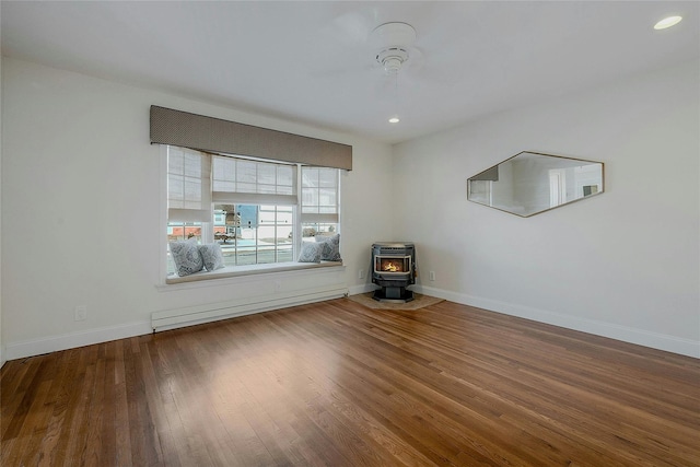 unfurnished room featuring baseboard heating, ceiling fan, hardwood / wood-style flooring, and a wood stove