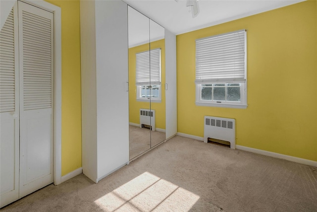 unfurnished bedroom with light colored carpet and radiator heating unit