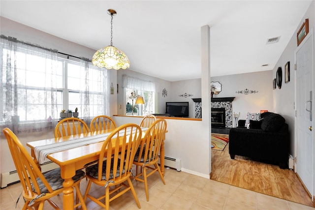 dining area featuring a tile fireplace, light tile patterned floors, and a baseboard heating unit