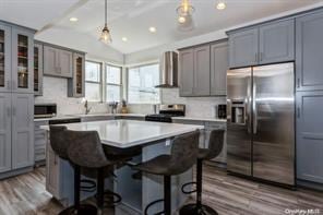 kitchen featuring appliances with stainless steel finishes, wall chimney exhaust hood, decorative light fixtures, a kitchen bar, and a center island