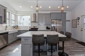 kitchen with pendant lighting, wall chimney range hood, appliances with stainless steel finishes, and a center island