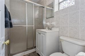 bathroom with a shower with door, toilet, vanity, and tile walls