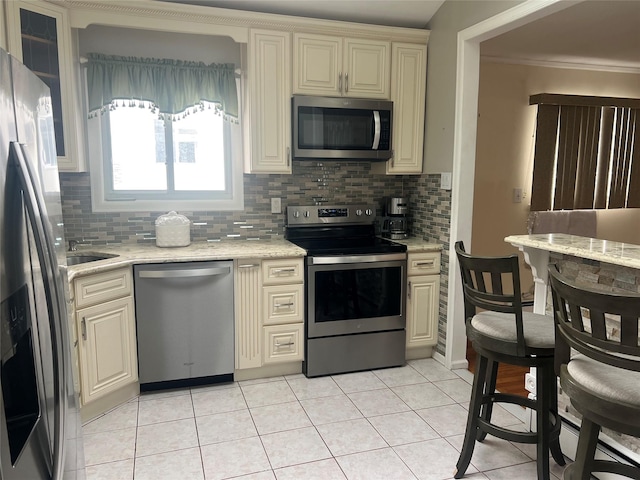 kitchen with cream cabinets, tasteful backsplash, light tile patterned floors, stainless steel appliances, and light stone counters