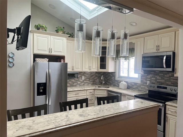 kitchen with hanging light fixtures, appliances with stainless steel finishes, sink, vaulted ceiling with skylight, and a breakfast bar area