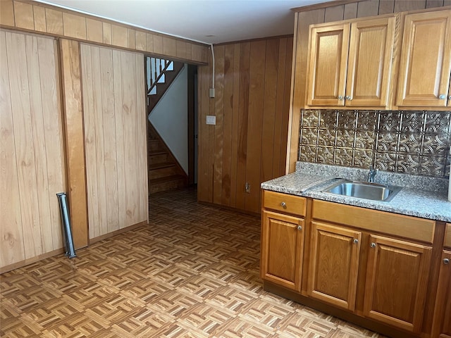 kitchen featuring light parquet floors, wood walls, light stone counters, and sink