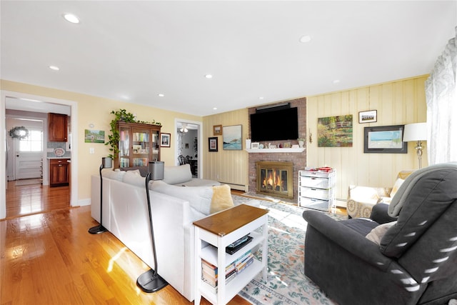 living room with a baseboard radiator, a brick fireplace, and light hardwood / wood-style floors