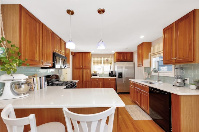 kitchen featuring black appliances, sink, hanging light fixtures, light hardwood / wood-style floors, and kitchen peninsula