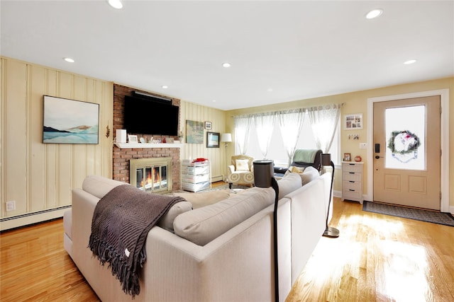 living room with a brick fireplace, a baseboard heating unit, and light hardwood / wood-style floors