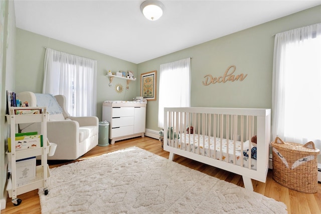 bedroom featuring a crib, a baseboard radiator, hardwood / wood-style floors, and multiple windows