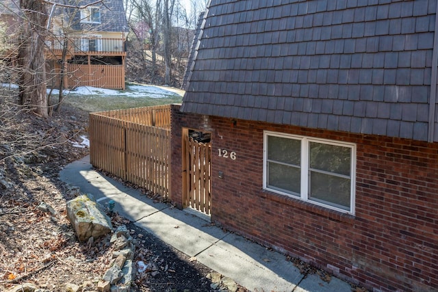 view of side of home with mansard roof, brick siding, and fence