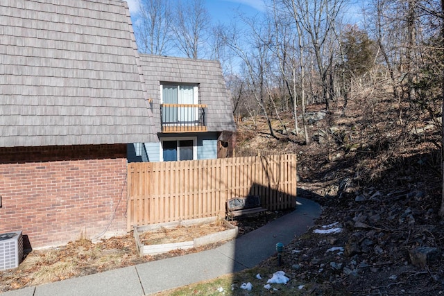 view of home's exterior featuring mansard roof, brick siding, central AC unit, and fence