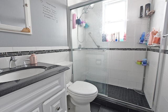 bathroom featuring toilet, tile walls, tile patterned floors, vanity, and a shower with door