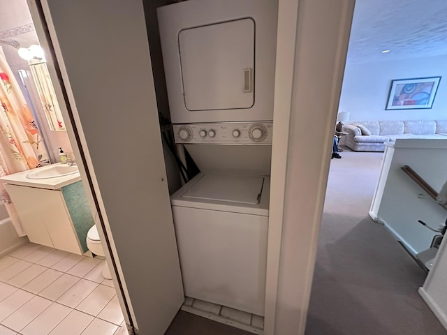 laundry area with sink, light tile patterned floors, and stacked washer and clothes dryer