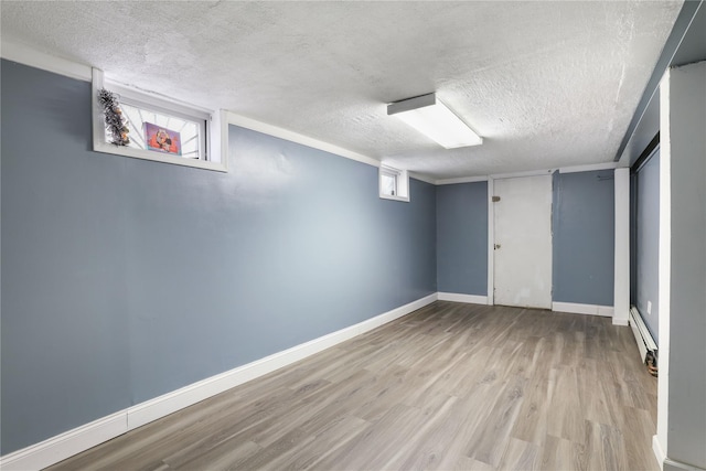 basement featuring a baseboard heating unit, a textured ceiling, and light wood-type flooring