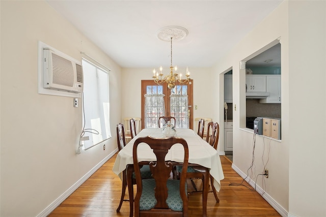 dining space with light wood-type flooring, an AC wall unit, and a notable chandelier