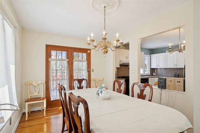 dining space featuring a healthy amount of sunlight, light wood-type flooring, and a notable chandelier