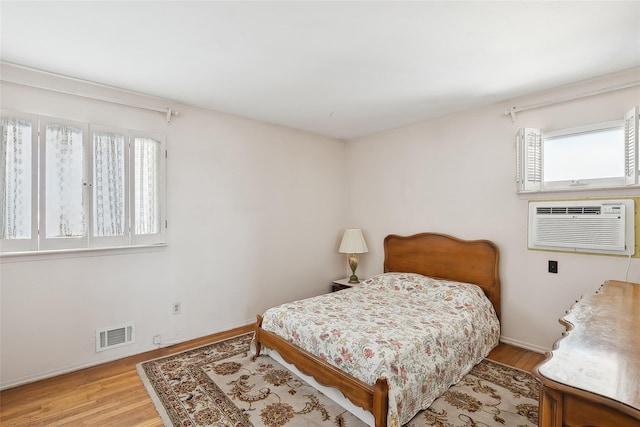 bedroom with a wall mounted AC, light hardwood / wood-style floors, and multiple windows