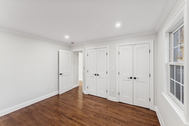 unfurnished bedroom with dark wood-type flooring, ornamental molding, and multiple closets